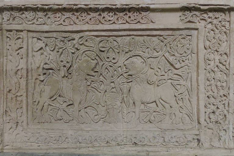 Transenna della scala della cripta, Due leoni che si fronteggiano fra tralci di uva uniti al centro da un mascherone (decorazione plastica) - ambito lombardo (secc. XI/ XII)