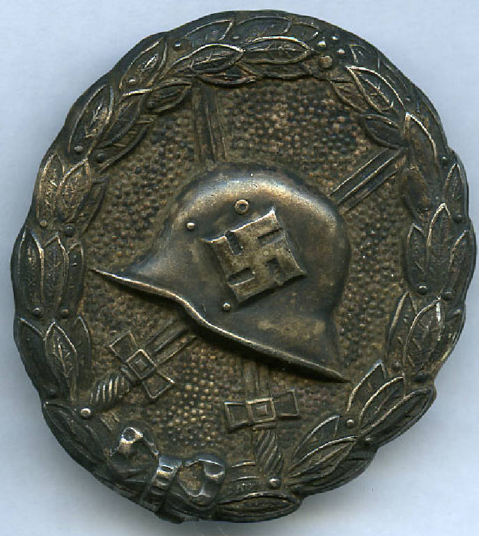 Distintivo delle Forze Armate tedesche per feriti della Seconda Guerra Mondiale, elmetto tedesco con svastica, spade e corona d'alloro (distintivo) - produzione (sec. XX)