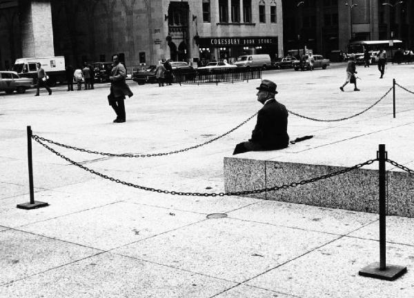 Anziano seduto sul basamento di un monumento al centro di una piazza