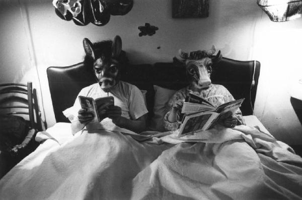 Ritratto di coppia a letto - uomo con maschera di asino, donna con maschera di mucca leggono