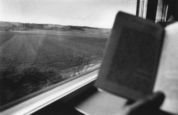 Veduta della campagna dal finestrino di un treno; mano regge libro in primo piano