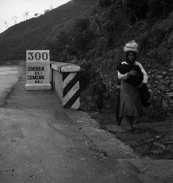 Italia del Sud. Calabria - strada - pietra miliare con le distanze verso Soveria e Catanzaro - donna con sporta in testa