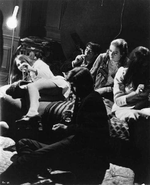 Ritratto. Foto di scena del film Blow-Up. David Hammings seduto a terra. Quattro ragazzi seduti su un divano fumano e bevono
