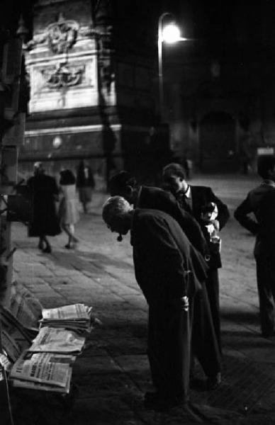 Italia del Sud. Napoli - piazza San Domenico Maggiore - rivendita di giornali - uomini leggono i titoli dei quotidiani esposti - notturno