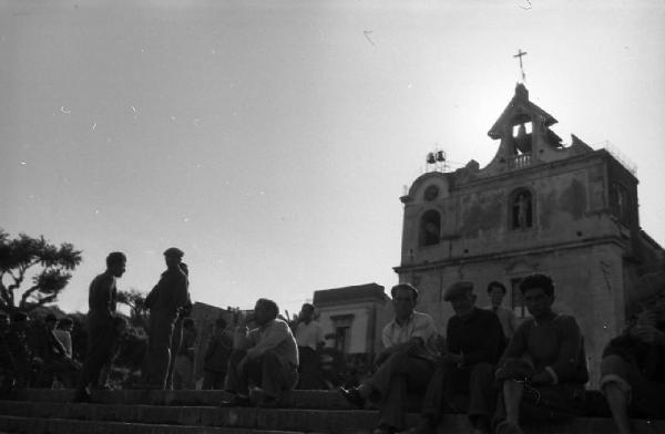 Italia del Sud. Acitrezza - piazza principale - uomini seduti sui gradini della scalinata - facciata della chiesa di San Giovanni Battista