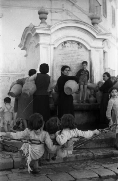 Italia del Sud. Gravina in Puglia - fontana dell'Isola o Pozzo Pateo - donne alla fonte - bambini di spalle appoggiati alla catena