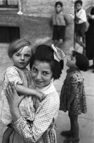Italia Dopoguerra. Periferia di Milano, le case popolari del quartiere "Baia del Re". Ritratto di coppia, una bambina che tiene in braccio la sorellina