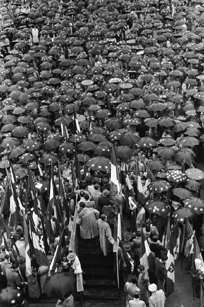 Referendum 1946 Repubblica o Monarchia. Milano - Piazza del Cannone - Manifestazione monarchica - Folla riparata sotto ombrelli con adesivi del tricolore monarchico - Bandiere