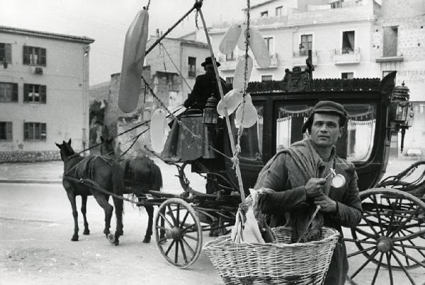 Sud Italia - esterno - uomo con cesto di vimini - palloncini - in secondo piano carro funebre con cavalli
