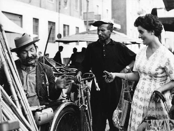 Fiera di Sinigaglia. Milano - Mercatino - Ritratto di gruppo - Rigattiere con baffi lunghi contratta con donna - Uomo con bici sullo sfondo