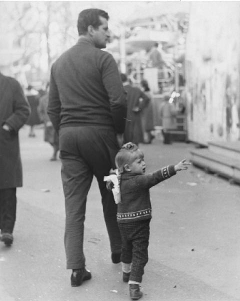 Luna park. Milano - Luna park - Uomo con bambina con treccia indica banchetto zucchero filato -- Giostre sullo sfondo