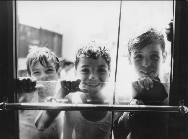 Napoli: Scugnizzi, si gioca. Napoli - Esterno - Ritratto di gruppo - Tre bambini appesi sul retro del tram con le mani sul vetro del finestrino