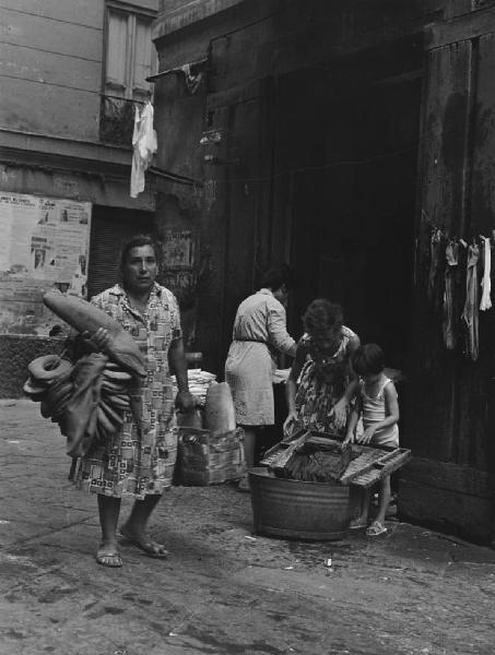 Napoli: Commercio. Napoli - Vicoli - Venditore ambulante di pane: donna - Donne e bambina in attività domestiche: bucato