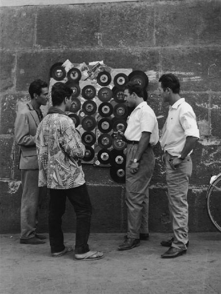 Napoli: Lavoro. Napoli - Vicoli - Uomini davanti alla bancarella di un venditore ambulante di dischi lp al muro - Ragazzi