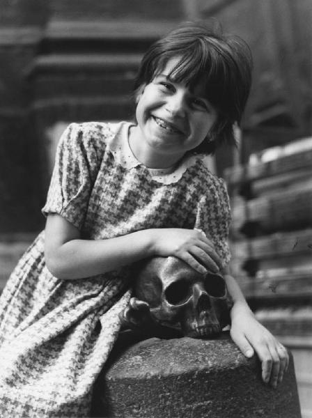 Napoli: Scugnizzi, figure, personaggi. Napoli - Vicoli - Ritratto infantile - Bambina abbraccia un paracarro con teschio in bronzo