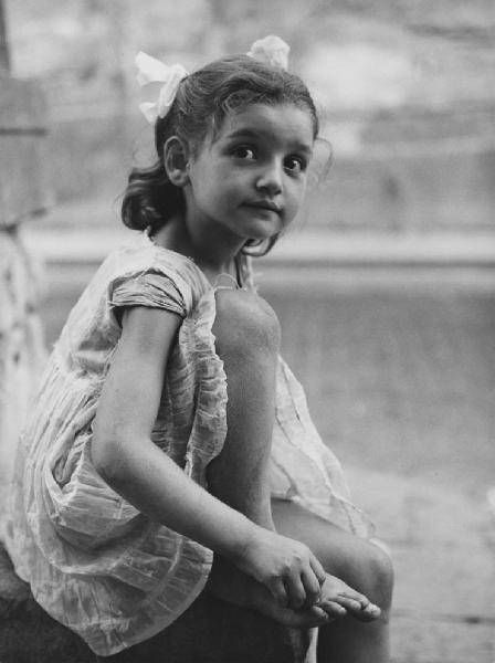 Napoli: Scugnizzi, figure, personaggi. Napoli - Vicoli - Ritratto infantile - Bambina seduta con gamba piegata, mano sul piede