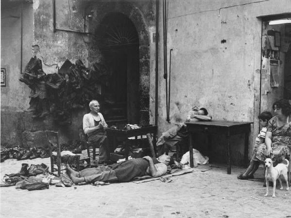 Napoli: Riposo/ Lavoro. Napoli - Vicoli - Banco di un calzolaio - Anziani a terra e al tavolo - Calzature, scarpe - Riposo - Cane