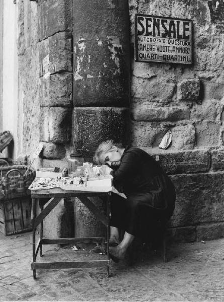 Napoli: Riposo. Napoli - Vicoli - Ritratto femminile - Donna anziana, venditore ambulante seduta al banco con merci - Riposo