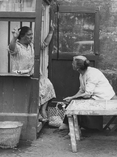 Napoli: Incontri scontri. Napoli - Vicoli - Ritratto femminile - Anziana con braccia alzate e anziana a un tavolo con fave