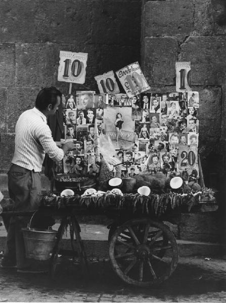 Napoli: Si vende si compra. Napoli - Vicoli - Venditore ambulante di cocco fresco: uomo - Banchetto: carretto con immagini divi del cinema