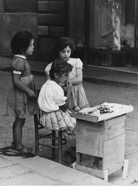 Napoli: Scugnizzi, si lavora/ Scene di vita varie. Napoli - Vicoli - Ritratto di gruppo - Bambine davanti a banchetto - Vendita cibo