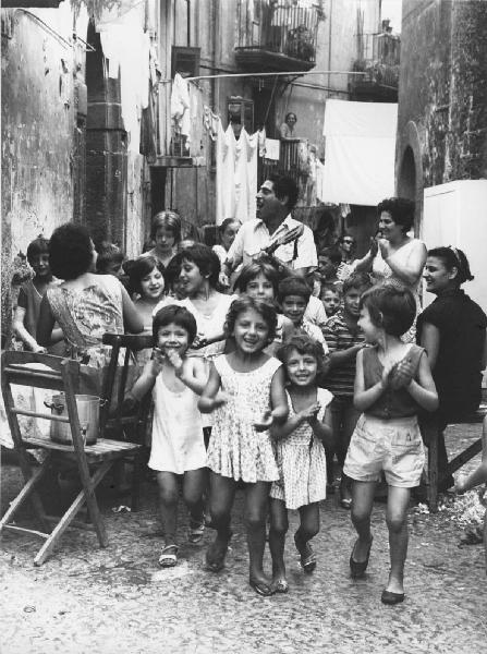 Napoli: Ci si diverte. Napoli - Vicoli - Ritratto di gruppo - Corteo di bambini con musicista - Chitarra - Musica, canto