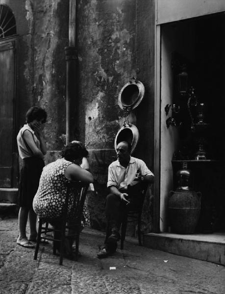Napoli: Conversazioni. Napoli - Vicoli - Ritratto di coppia - Coppia seduti su sedie e ragazza in piedi - Conversazione