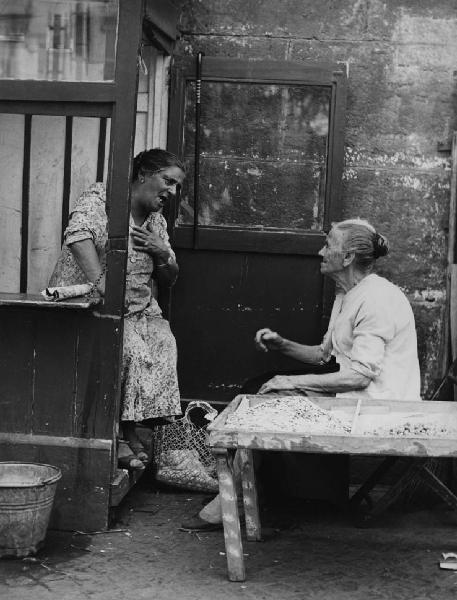 Napoli: Conversazioni. Napoli - Vicoli - Ritratto femminile - Anziana con bocca aperta e mano al petto con anziana seduta a un banchetto con fave