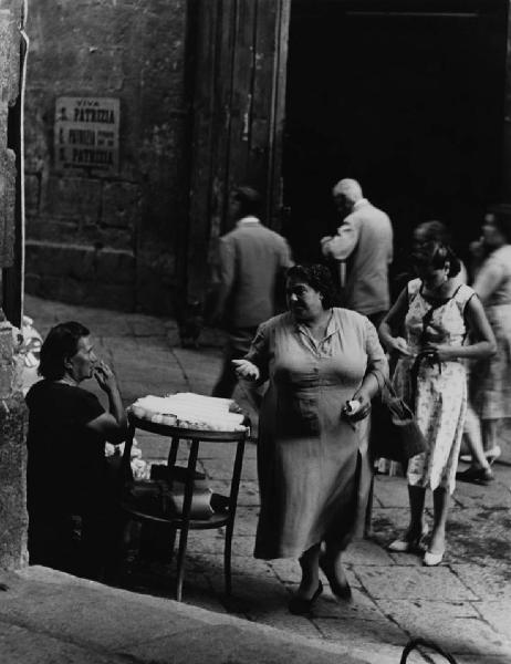 Napoli: Conversazioni. Napoli - Vicoli - Venditore ambulante: anziana seduta al banco con merci, oggetti - Anziana