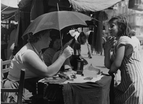 Napoli: Conversazioni. Napoli - Vicoli - Venditore ambulante al banco con merci: donna - Ragazza - Ombrello, ventaglio