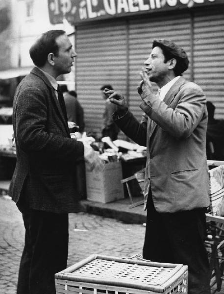 Napoli: Conversazioni. Napoli - Strada - Ritratto maschile - Uomo venditore ambulante parla con altro uomo - Gestualità delle mani