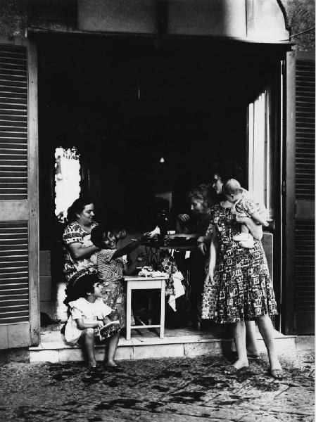 Napoli: Scene di vita varie. Napoli - Vicoli - Donne con bambini e neonato sull'uscio di casa - Sarta, macchina da cucire