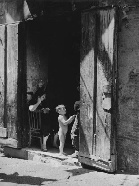 Napoli: Scene di vita varie. Napoli - Vicoli - Ritratto di famiglia - Donna seduta su una sedia sull'uscio di casa con bambino nudo: pianto - Ragazzino