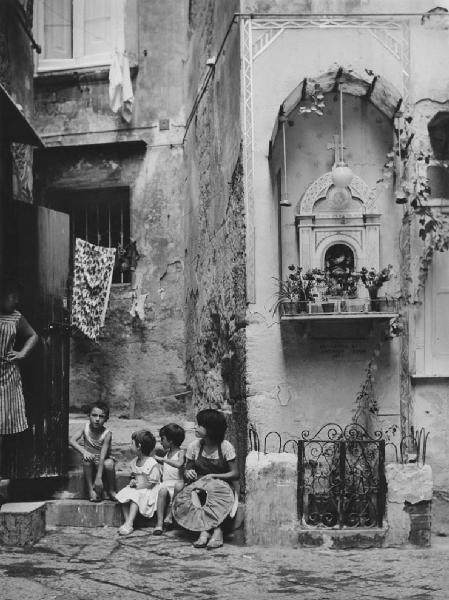 Napoli: Scene di vita varie. Napoli - Vicoli - Edicola votiva - Bambini seduti su dei gradini - Donna in piedi sull'uscio di casa