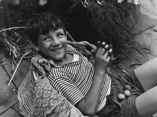 Napoli: Scene di vita varie. Napoli - Ritratto infantile - Bambino a terra appoggiato a una cesta di vimini - Fichi