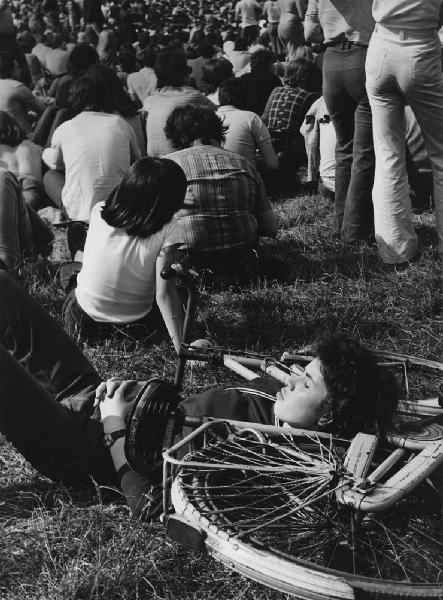 Festival Pop. Milano - Parco Lambro - Festival pop - Ritratto maschile - Ragazzo sdraiato nel prato sopra bicicletta - Folla in secondo piano