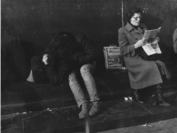 Piazza Duomo: Amore. Milano - Piazza del Duomo - Monumento a Vittorio Emanuele II - Ritratto di gruppo - Coppia di ragazzi seduti: abbraccio, bacio - Anziana con giornale