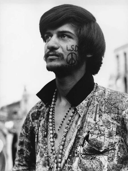 Mondo Beat: Volti figure. Milano - Piazza del Duomo - Ritratto maschile - Ragazzo con tatuaggio sul volto: peace, L.S.D - Droghe
