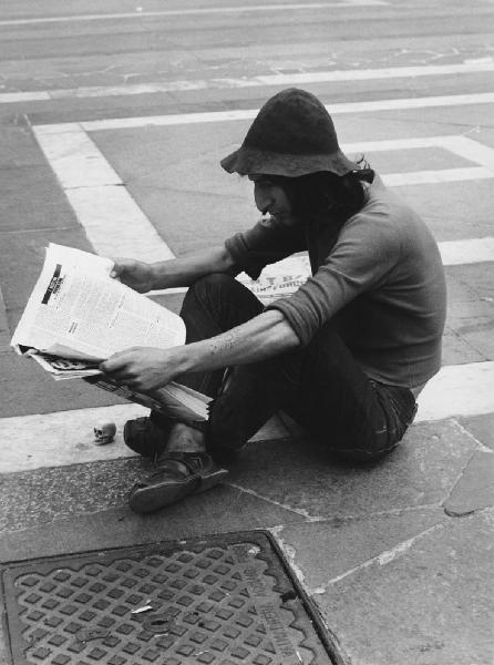 Mondo Beat. Milano - Piazza del Duomo - Ritratto maschile - Ragazzo seduto a terra con cappello, tatuaggio e giornale - Lettura - Teschio miniatura