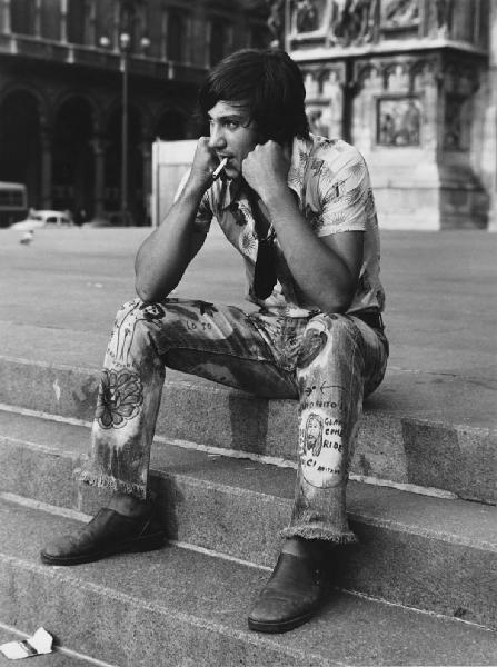 Mondo Beat. Milano - Piazza del Duomo - Ritratto maschile - Ragazzo seduto sui gradini - Sigaretta e jeans con scritte
