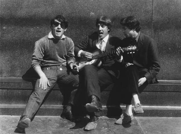 Mondo Beat. Milano - Piazza del Duomo - Monumento a Vittorio Emanuele II - Ritratto di gruppo - Ragazzo con chitarra con due ragazzi: canto, occhiali da sole, sigaretta