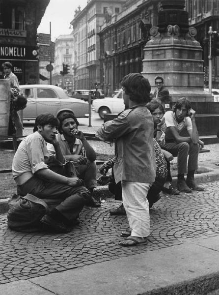 Mondo Beat. Milano - Piazza del Duomo - Ragazzi seduti su ringhiera dell'aiuola e nano in piedi