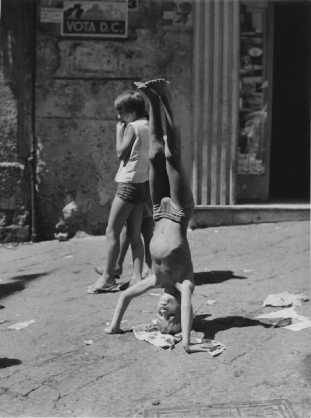 Napoli: Bimbi, scene di vita varie. Napoli - Vicoli - Ritratto infantile - Bambino in costume da bagno: verticale - Manifesto politico sullo sfondo