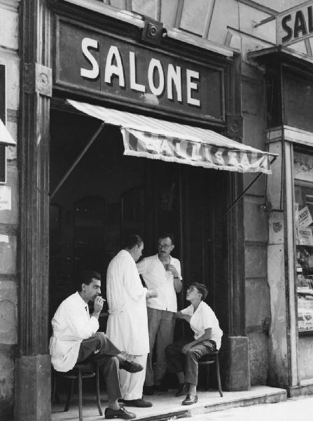 Napoli: Seconda scelta. Napoli - Strada - Salone callista - Uomini in camice e uomo in borghese con bambino sull'ingresso del negozio
