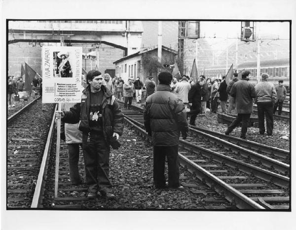 Manifestazione Alfa Romeo. Milano - Stazione Centrale - Manifestazione operaia Alfa Romeo - Occupazione binari - Gruppo di operai - Bandiere e cartello con riproduzione di Emiliano Zapata