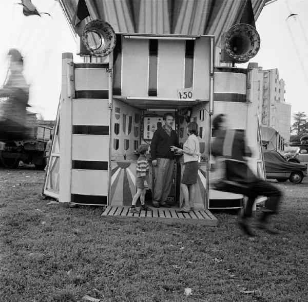 Milano, periferia - Via delle Forze Armate - Luna park - Giostra a seggiolini "calci in culo" - Ritratto di gruppo: uomo, donna e bambino - Uomo su seggiolino in movimento