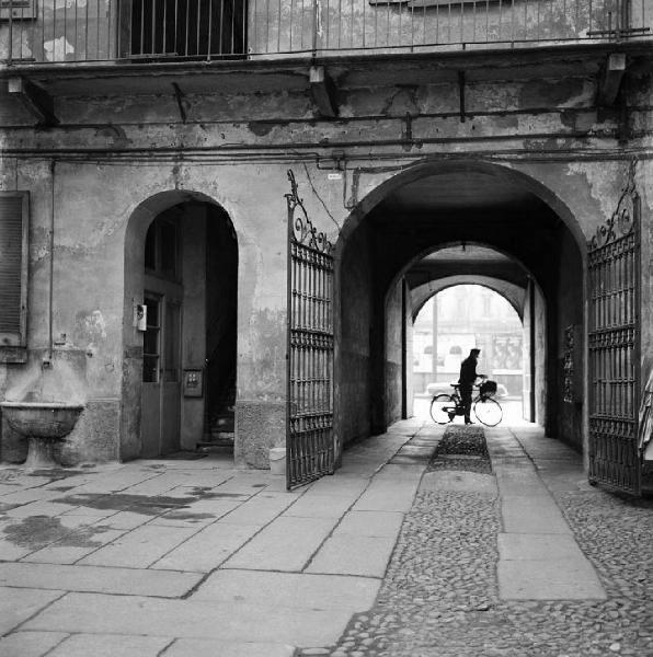 Milano - Via Montegrappa 16 - Casa di ringhiera, androne e cortile interno - Ritratto maschile: uomo con bicicletta - Cancello aperto