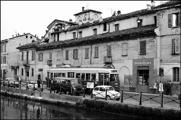 Milano - Via Lodovico Il Moro 11 - Naviglio Grande, sponda - Tram 19 - Osteria Olona -Drogheria - Negozio di legna e carbone - Merceria - Trattoria Moscone - Persone sul marciapiede - Furgone con scritta "macelleria polleria Sala"