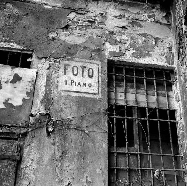 Milano - Via Madonnina 10 - Particolare di una parete deteriorata: insegna dipinta con scritta: "Foto 1° piano", finestra con sbarre in ferro
