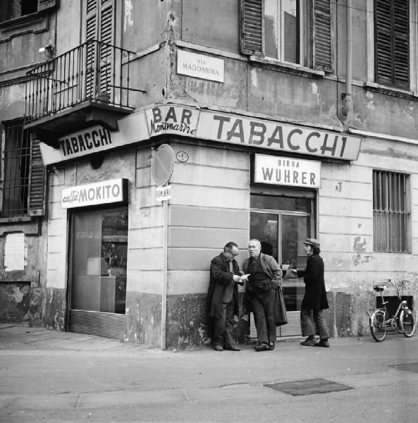 Milano - Via Madonnina angolo via Fromentini - Bar Tabacchi Montmartre, esterno - Insegna del bar - Ritratto maschile di gruppo: uomini davanti all'ingresso del bar - Bicicletta - Insegna della birra Wurer - Insegna del caffè Mokito